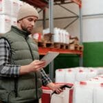 Pracownik hurtowni zarządza zapasami na tablecie między regałami magazynu