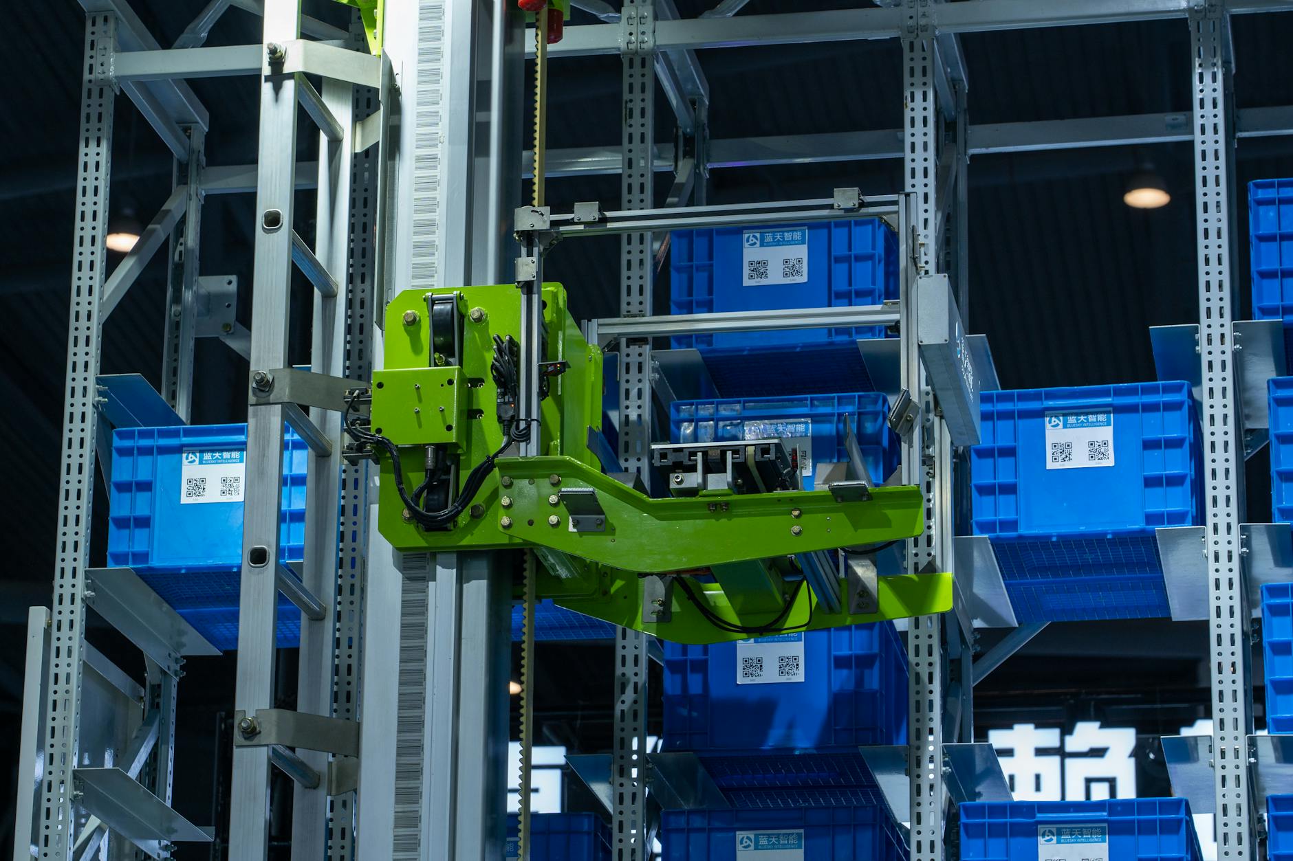Zielone ramię robota odkłada niebieskie skrzynki w zautomatyzowanej hurtowni
