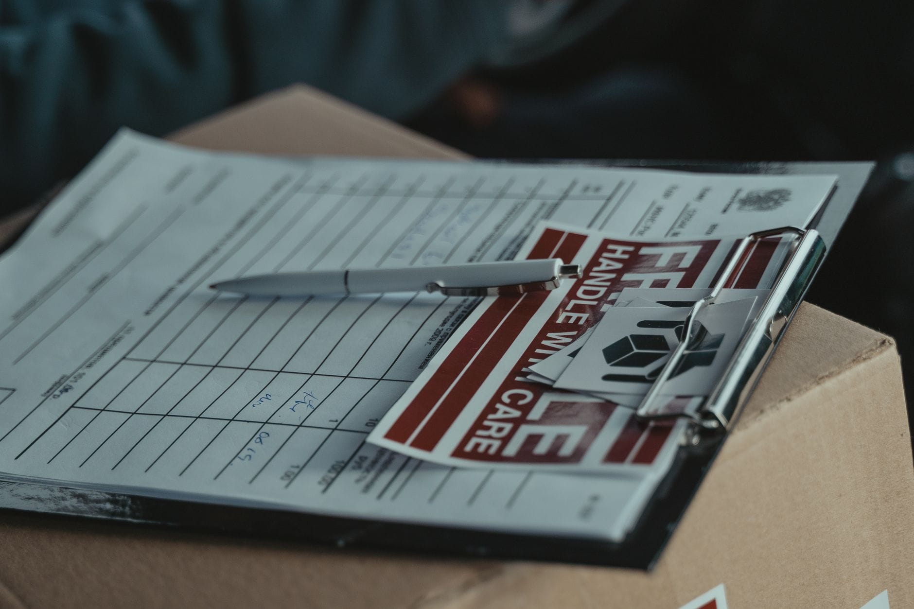 Clipboard z dokumentami dostawy na kartonie z naklejką Ostrożnie